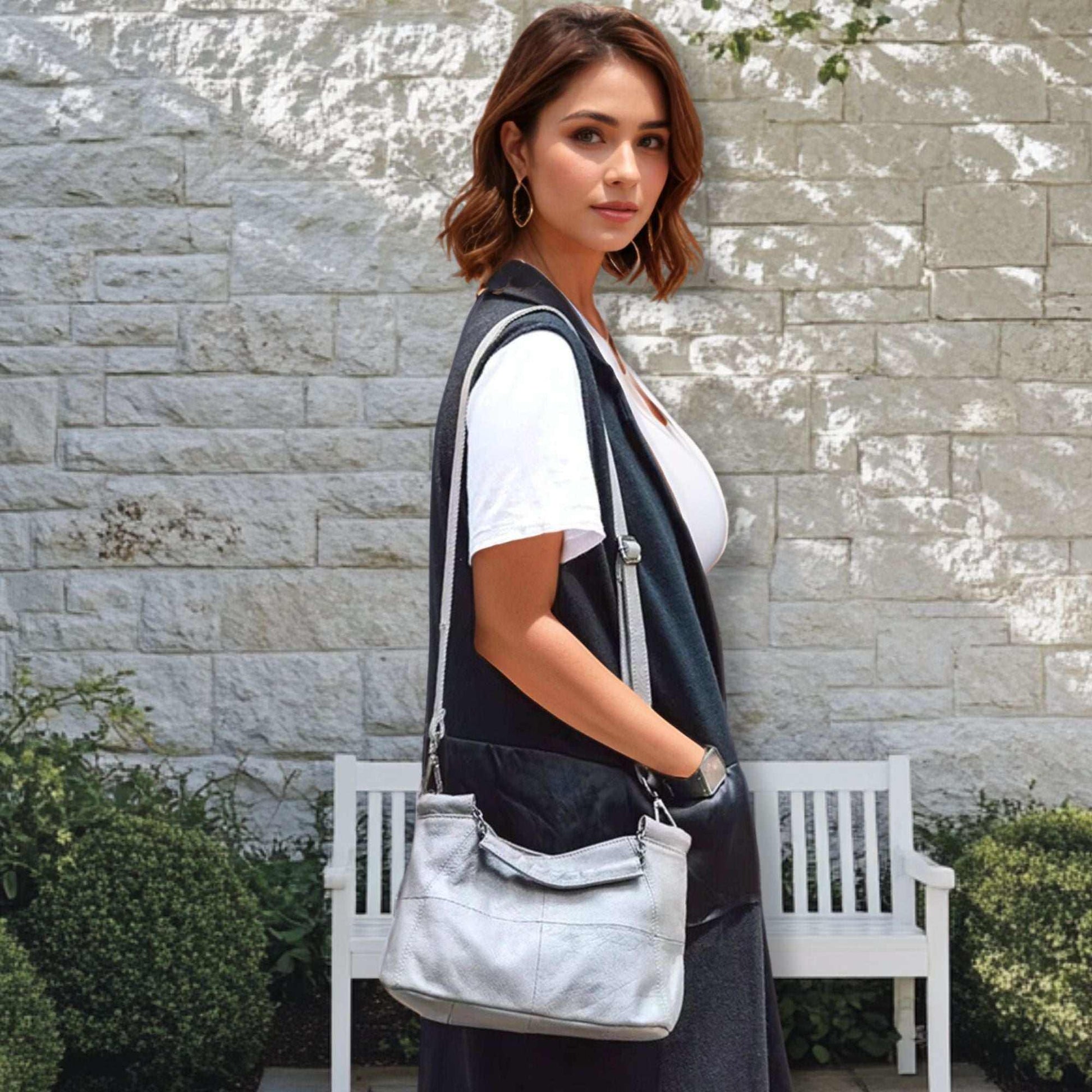 Stylish woman with Cross Body Soft Leather Bag in front of stone wall and greenery.