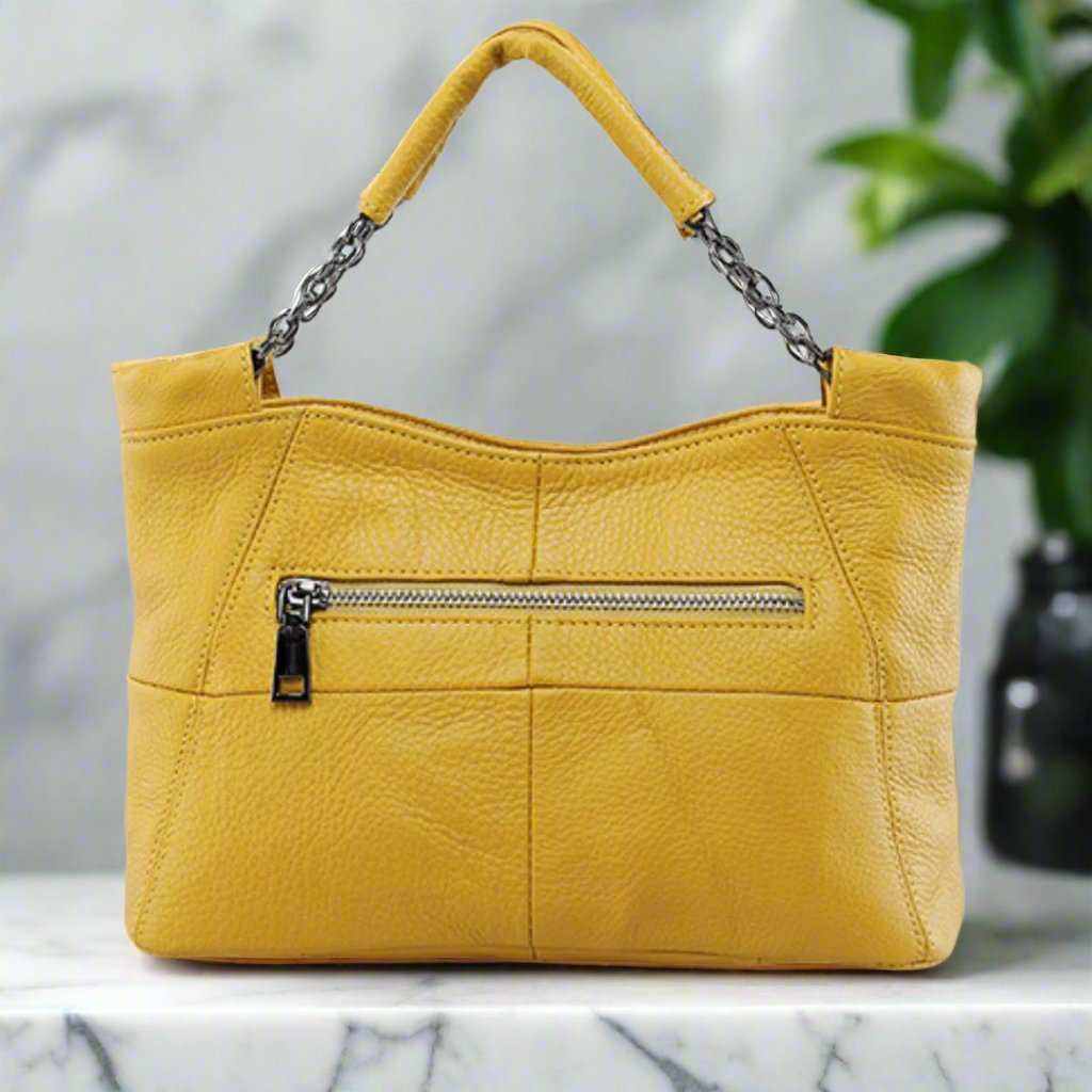 Yellow crossbody soft leather bag with chain-link handle and front zipper pocket on marble surface.