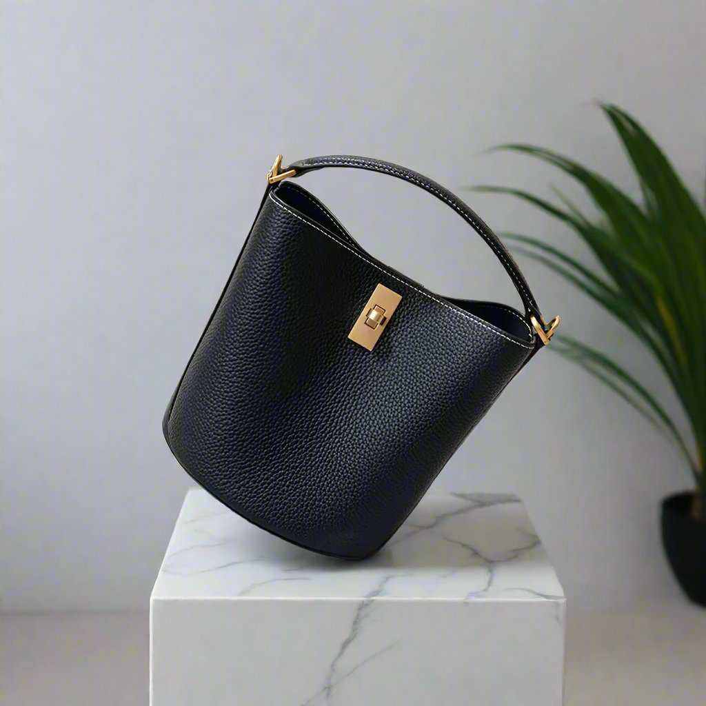 Black leather crossbody bucket purse on a marble surface.