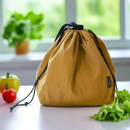 Insulated lunch pouch with drawstring closure on a table, surrounded by fresh vegetables.