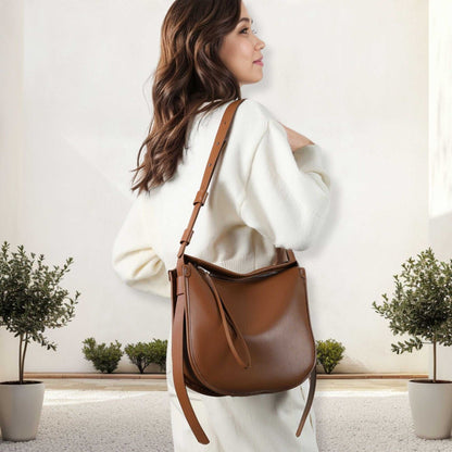 Large Crossbody Satchel in brown leather, worn by a woman in a white outfit, showcasing its sleek design and adjustable strap.