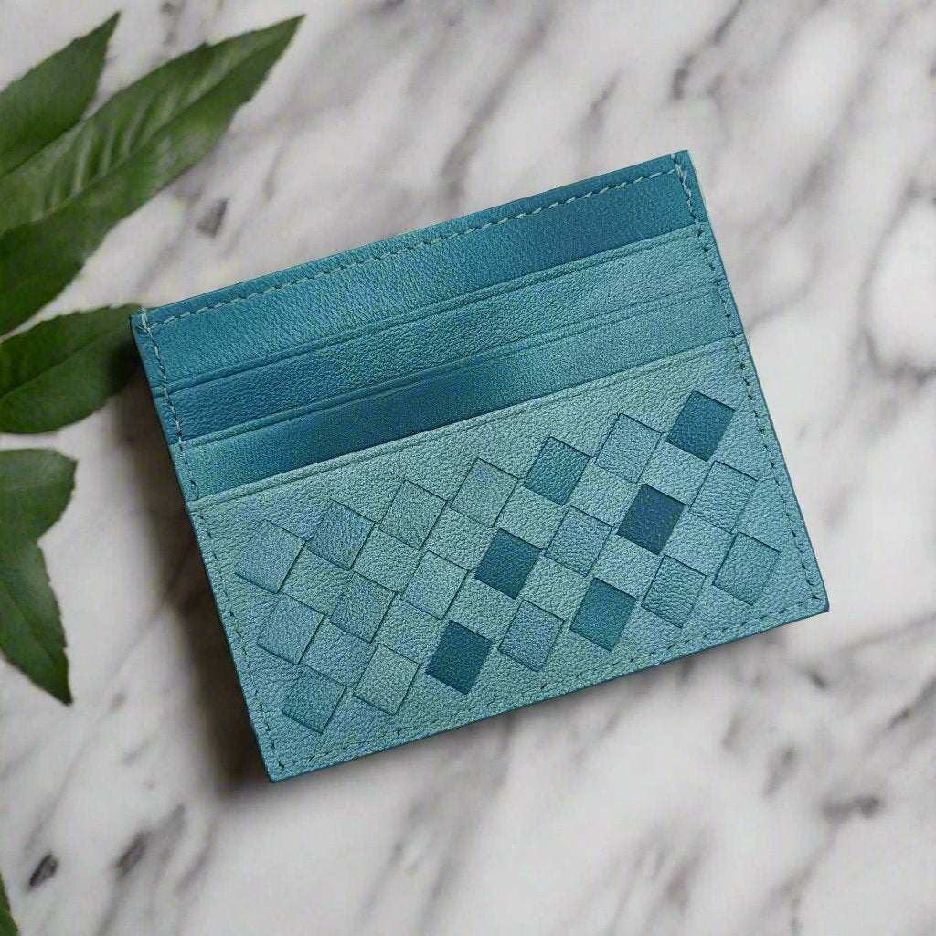 Bold blue leather credit card carrier with woven design on a marble surface.