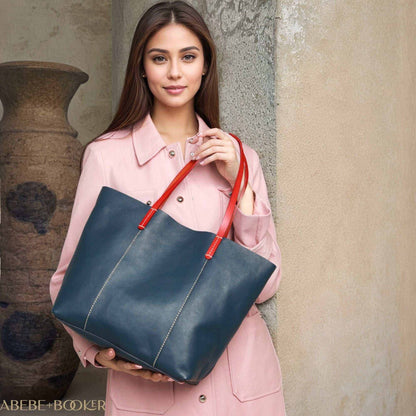 Blue leather handbag with red straps from the Essence of Elegance Collection, held by a woman in a pink coat.