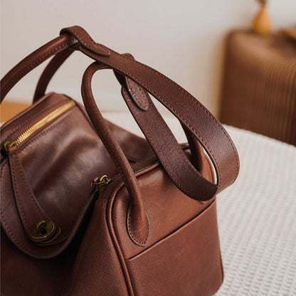 Brown Leather Satchel Purse with handles and gold hardware on a textured surface.