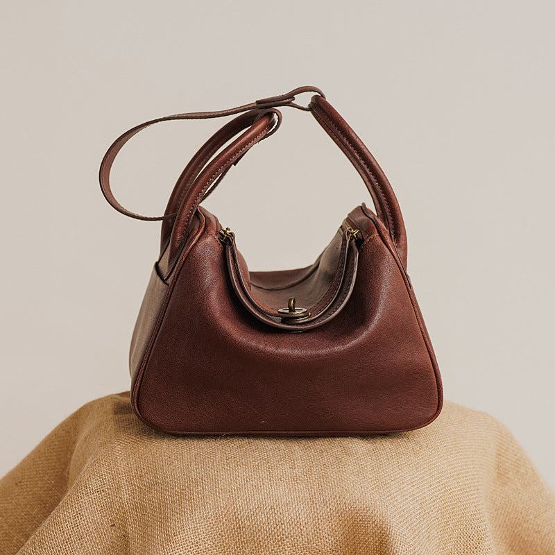 Brown leather satchel purse with adjustable strap on display.