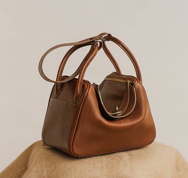 Brown leather satchel purse with straps and secure zipper closure.