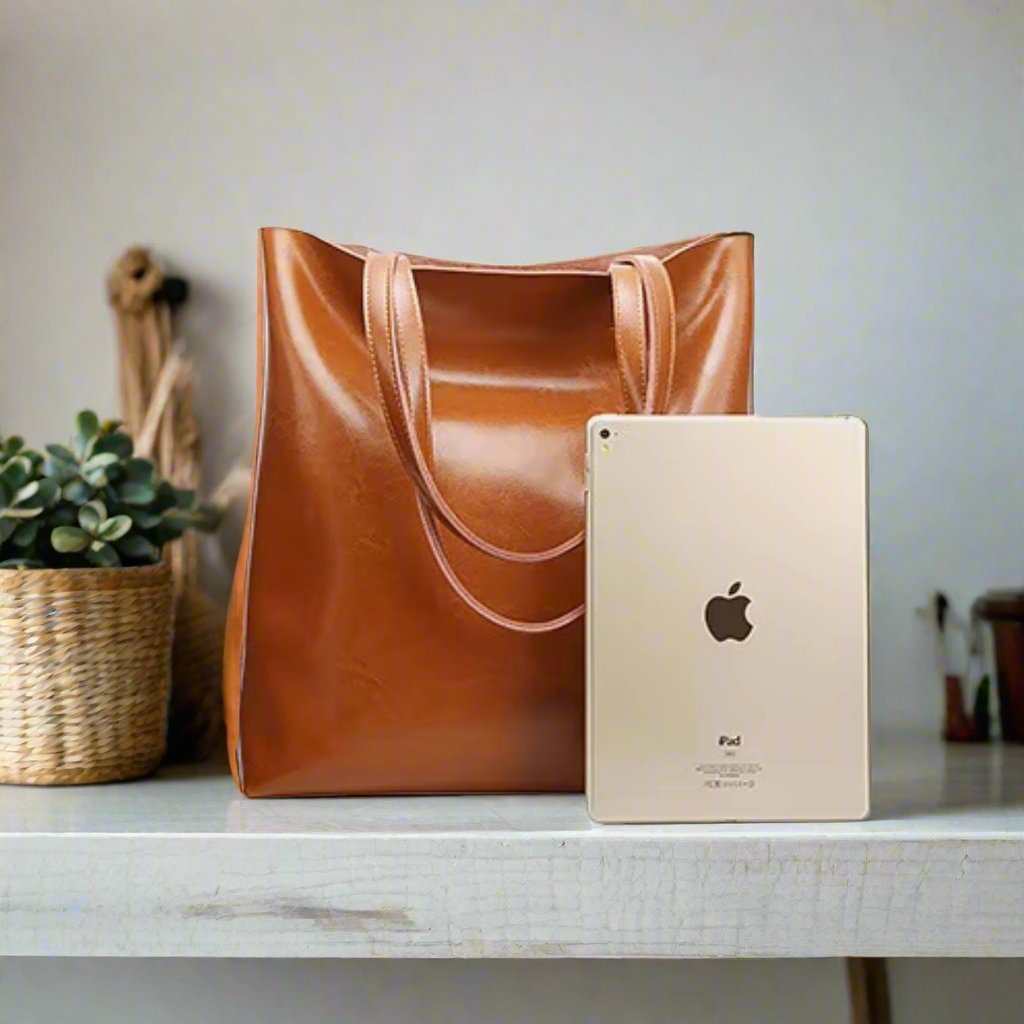 Leather shoulder bag with iPad for scale on table.