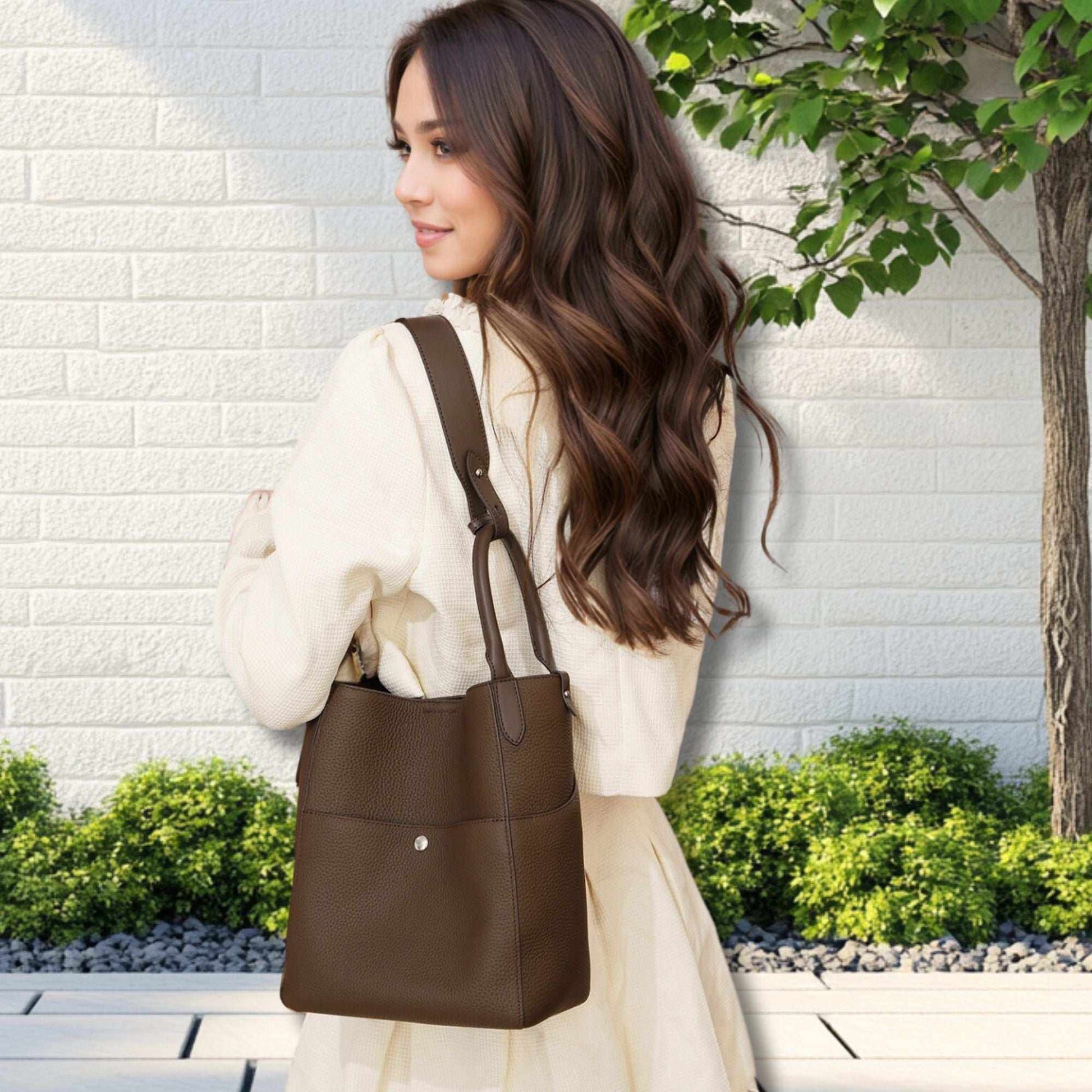 Leather tote bag crossbody in brown, worn by a woman, showcasing its versatile bucket design and dual handle straps.