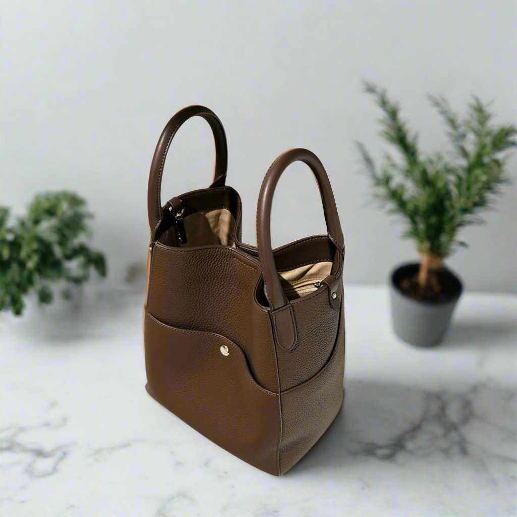 Elegant brown leather tote bag with dual handles, placed on a marble surface, featuring a spacious interior and crossbody capability.