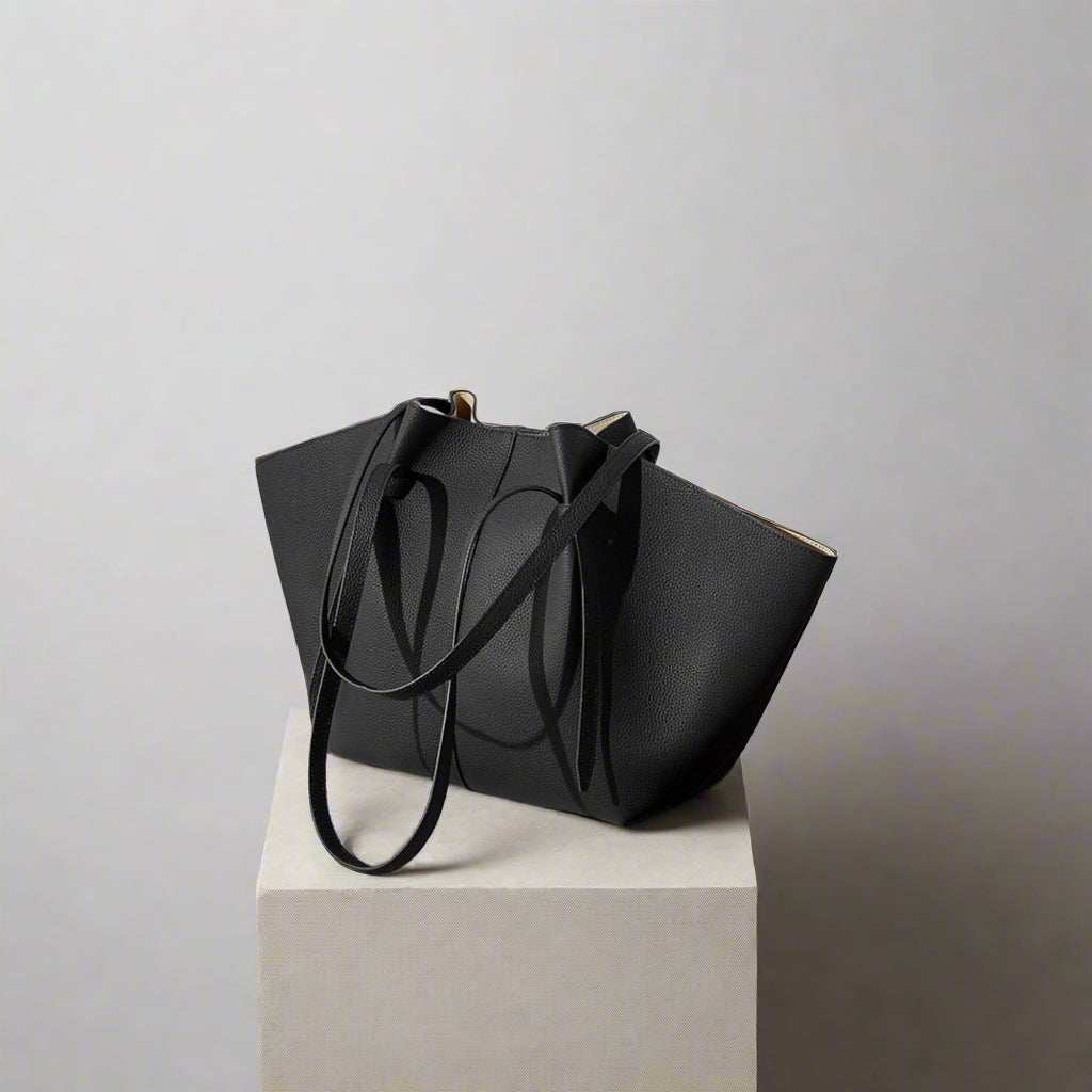 Black leather work tote with pleated strap design on a pedestal.