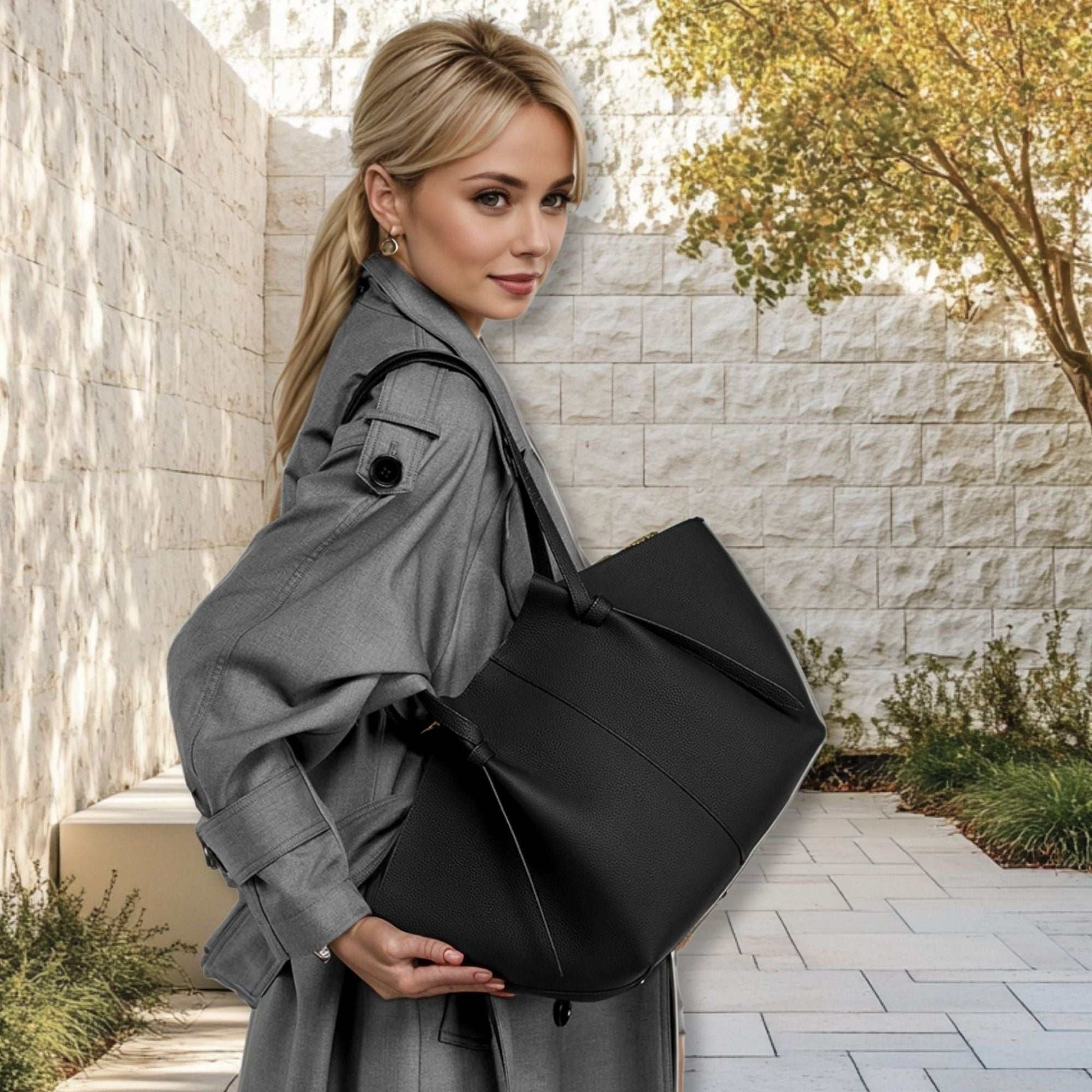 Black leather work tote with pleated straps, carried by a woman outdoors.