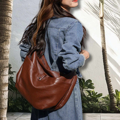 Woman carrying a brown slouchy leather handbag wearing a denim jacket.