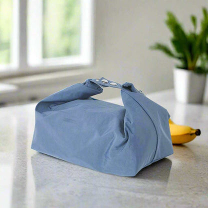 Small lunch bag in a light color on a countertop with a banana in the background.