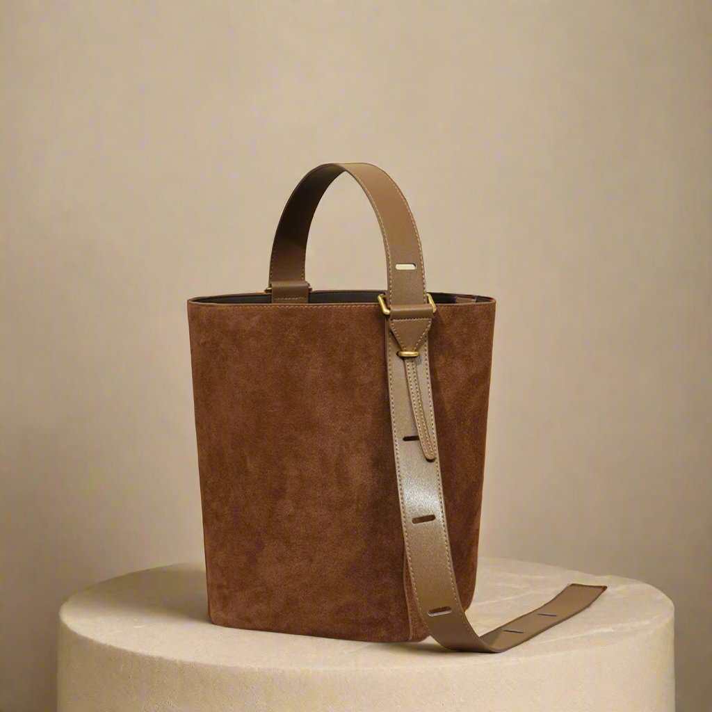 Suede bucket bag with adjustable strap on a neutral background, showcasing sleek design and rich texture.