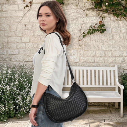 Woven leather crossbody bag in black, worn by a woman outdoors.